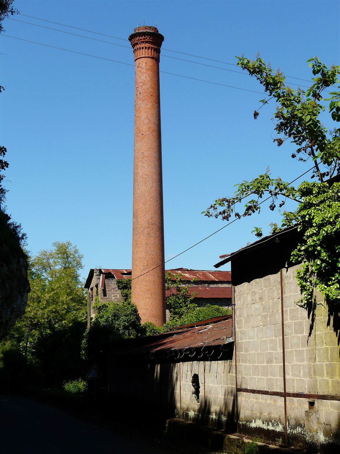 Haute cheminée de brique d'une ancienne papeterie, dressée au-dessus des toits des anciens ateliers.