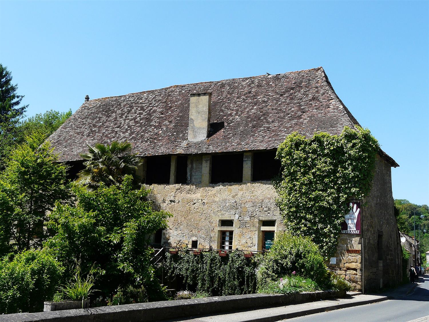 Le moulin de Larroque vu depuis la route : long bâtiment de pierre à deux niveaux, façade couverte de végétation.